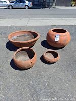 Four garden round terracotta pots displayed outdoors on asphalt in daylight, showing various angles and surface details.