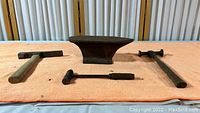 Set of one iron anvil and three metalworking hammers laid out on an orange cloth showing full items