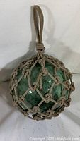 Front view of blue-green glass orb inside tan rope net with loop handle