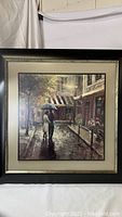 Front view of the framed art print showing the couple walking under an umbrella on a rainy city street, with clear visibility of frame condition and artwork details.