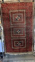 Full view of the red Persian area rug with three large square medallions and multi-layered borders hung vertically.