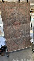 Full view of tan and red Persian style rug showing overall wear, fading, and frayed edges.