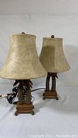 Pair of wooden palm tree table lamps with beige shades side by side showing full view