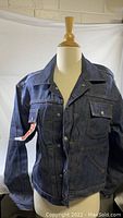 Front view of dark blue denim jean jacket on mannequin, showing snap button front and chest pockets.