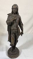 Front view of vintage metal statue of historical male figure with detailed clothing and hand on chest.