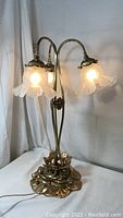 Full view of the vintage three-bulb gooseneck tulip table lamp with all lamps lit, showing frosted glass shade shape and metal base details