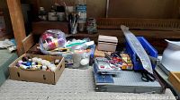 Photo of assorted art and office supplies including paints, paper cutter, scissors, pliers, colored pencils, and ties laid on carpet