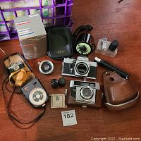 Photo displaying cameras, lens, light meter, flash, and accessories on a wooden surface