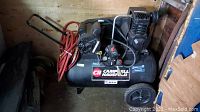 Full view of the Campbell Hausfeld air compressor showing tank, motor, handle, wheels, and attached red air hose.