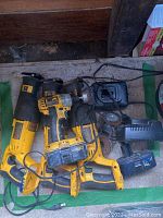 Photo showing two Dewalt reciprocating saws, a Dewalt impact driver with wire brush, and a Dewalt battery charger with battery pack on a concrete floor.