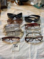 Top-down view of all nine pairs of eyeglasses and sunglasses arranged on white cloth with visible scratches and variety of frames.