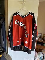Front view of red hockey jersey with 'Campbell' lettering across the chest and stars on sleeves.
