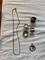 Full lot of sterling silver jewelry items including the broken chain, rings, and pendant arranged on cloth.