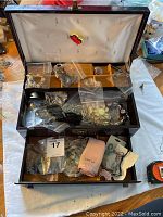 Open jewelry box showing divided compartments filled with assorted jewelry pieces in plastic bags and loose items.