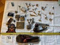 Full view of collection on white cloth showing pipes, pocket watches, lighters, cuff links, pins, badge patch and accessories with measuring tape for scale.