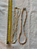 Two freshwater pearl necklaces laid flat next to a measuring tape showing approximately 18 inches in length.