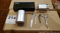 Two new manicure sets including silver-tone metal cylindrical cases and manicure tools: nail file, cuticle pusher, nail clippers, scissors shown laid out on cardboard.