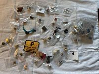 Overview photo showing many small pins, earrings, badges in plastic bags laid out on white fabric.
