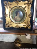 Framed Vienna art plate with portrait of a woman, ornate gold and black frame with decorative accents, and chips visible on the frame.