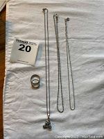 All items arranged on white surface: two silver wedding bands, silver necklace with cyclist pendant, two silver plated chains.