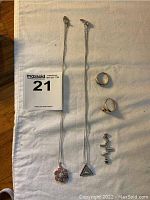 Photo of two silver necklaces laid flat next to two silver rings on white cloth background
