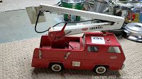 Red Tonka diecast fire truck with white extendable ladder sitting on a carpeted floor, showing side and top view of the vehicle.