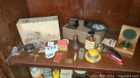 Shelf displaying an assortment of small collectible and trinket items including glass bottles, miniature helmet, cross pendant, knives, matchbox, and small boxes