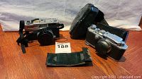 Two vintage Canon cameras with leather cases on wood floor showing front and side angles