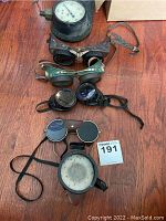 Overview of all four pairs of goggles and metal respirator mask on wood floor
