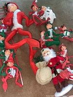 Photo showing all 13 dolls including Santa Claus with burlap sack and 12 elves in red and green outfits.