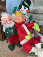Five festive dolls grouped together showing their faces and costumes, include Santas, snowmen, and elf
