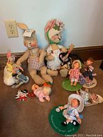 Photo showing large bunnies, smaller bunnies in Easter attire, mice figures, and child dolls on bases with various clothing and hats.