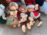 Three monkeys dolls in Santa hats and outfits holding burlap sacks