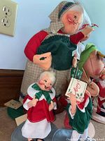 Photo showing large Santa doll with green apron and bonnet, and two smaller Santa dolls in red and green clothing holding a holiday sign