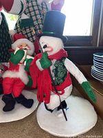 Close-up image of snowman doll and Santa doll with book showing detailed fabric and painted faces.