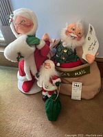 Photo of two Santa dolls and one Mrs. Claus doll standing on carpet, Santa sitting inside 'Santa's Mail' sack, cheerful holiday faces with fabric clothing and accessories.