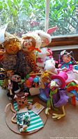 Photo showing most of the dolls including scarecrows, bunny, colorful jester doll, small character with balloons, purple bird-like doll, and cat on towel