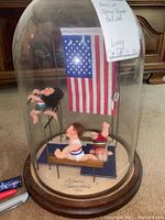 Front view of Annalee Special Olympics bell jar showing three gymnastics figures with American flag inside the dome on wooden base.