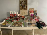 Overview of the collection of Coca-Cola memorabilia items laid out on a table including cups, trays, signage, pins, football, books, and other collectibles.