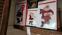 Three boxed Coca-Cola Santa Claus figurines and one small ornament displayed on a shelf.