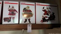 Three boxed fabric Coca-Cola Santa figurines displayed side by side.