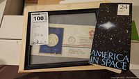 Framed first day of issue commemorative coin set including envelope and certificate with a 24-karat gold plated "America in Space" coin folder next to it.