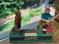Mechanical baseball coin bank with IBM award plaque on green base, showing three players in colorful uniforms