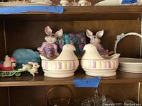 Shelf with two Lenox chick-shaped containers, pink rabbit figurines, blue dish, and ceramic basket with rabbit handles