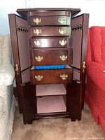 Photo of the tall wooden jewelry cabinet showing multiple brass-handled drawers, side doors with metal hooks, and lower storage doors open.