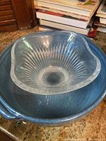 Photo of large blue ceramic bowl with clear glass decorative bowl inside, both placed on a granite countertop with books in the background.