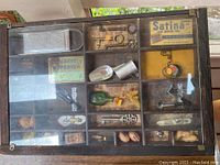 Top view of first wooden shadow box containing assorted small items and pins behind the glass front.