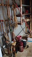 Photo showing a variety of long-handled garden tools such as shovels, pitchfork, rake, with rope, croquet set mallets and balls, and Chapin sprayer on floor.
