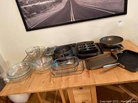 Glass mixing bowls, casserole dishes, baking pans, springform pan, mini Bundt pan, cast iron griddle, loaf pans and measuring cup on a wooden table
