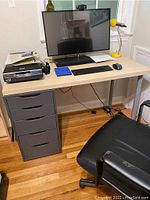 Photo showing assembled desk setup with Ikea Alex drawer unit in gray on left and Lagkapten desk top with legs in light wood tone. Keyboard, mouse, monitor, and lamp on desk surface for scale.